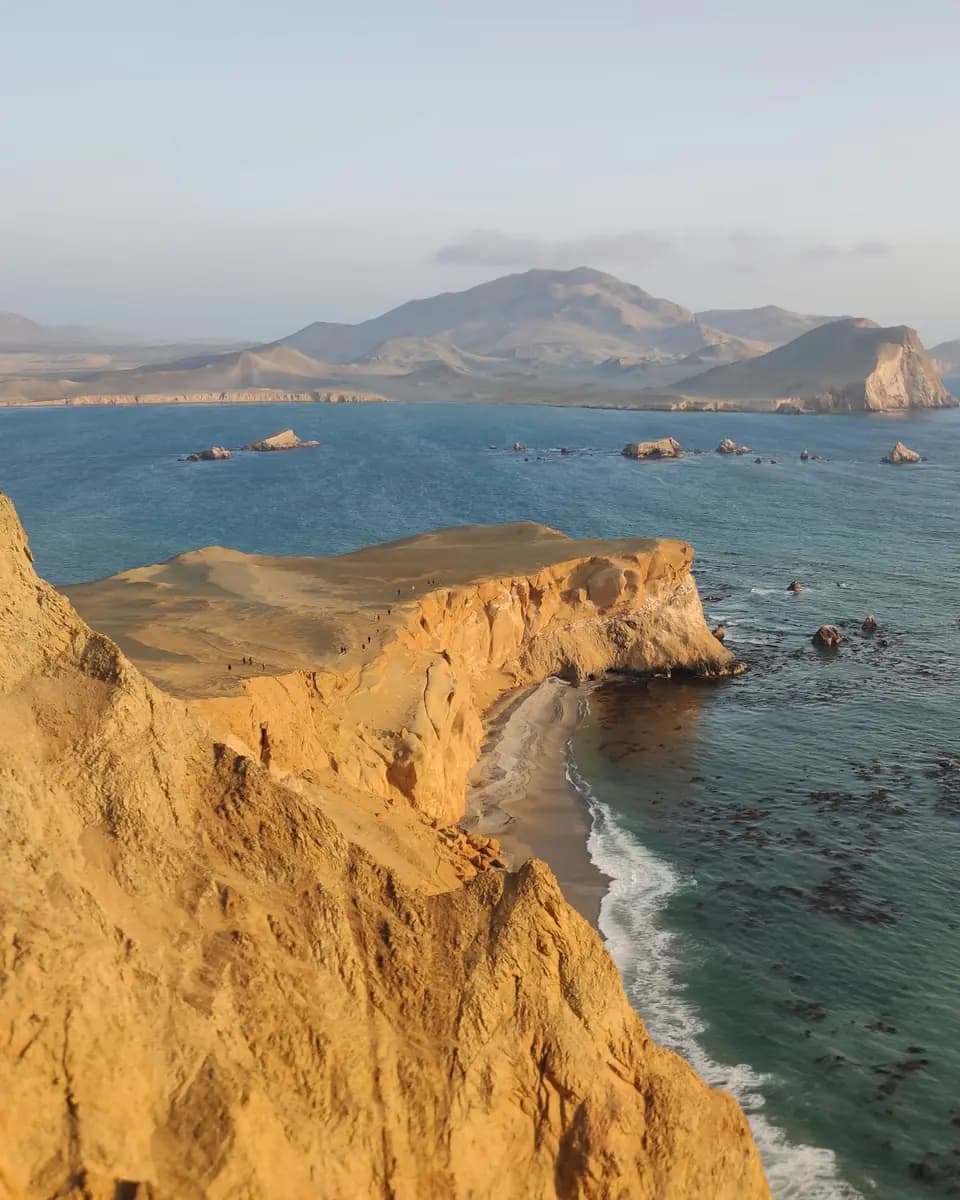 Golden desert cliffs descending to blue Pacific waters along the Paracas coast.