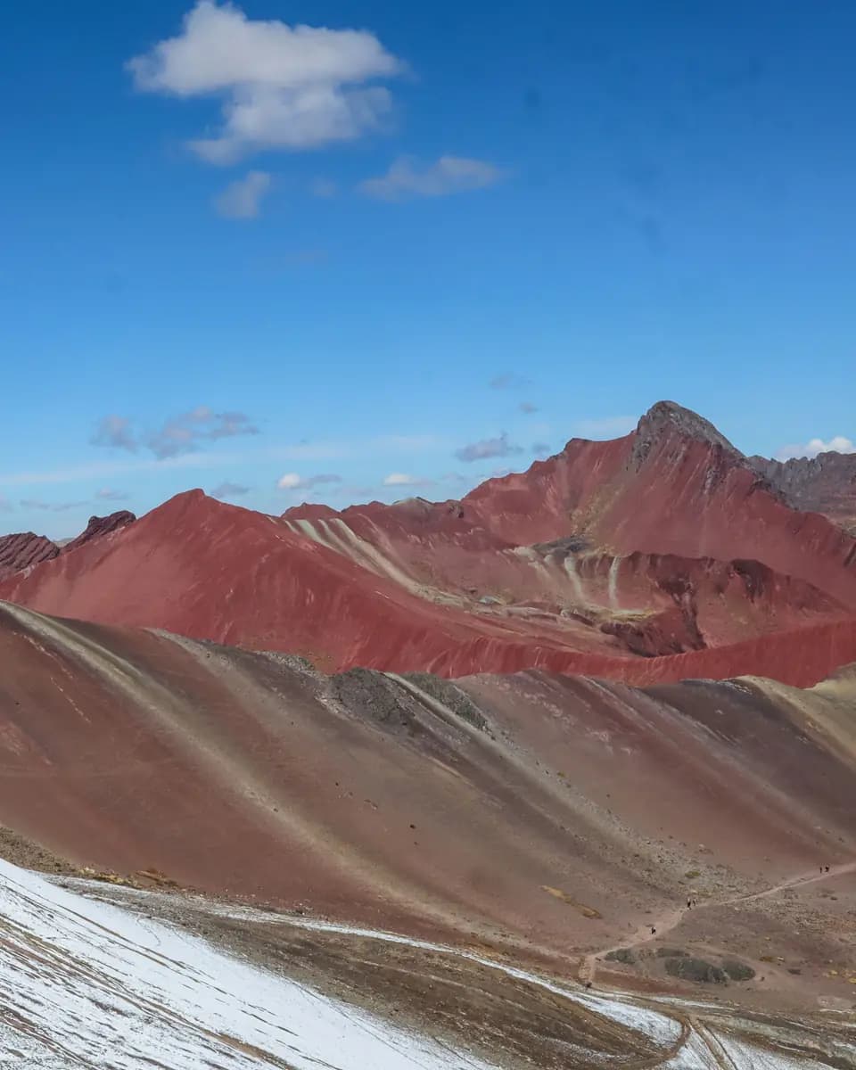 Layered red and mineral-colored ridges of Rainbow Mountain beneath a blue sky.
